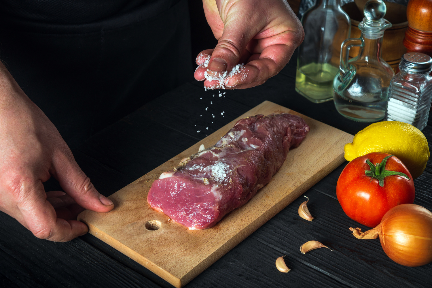 Chef or cook sprinkles the raw beef meat with salt. Preparing me